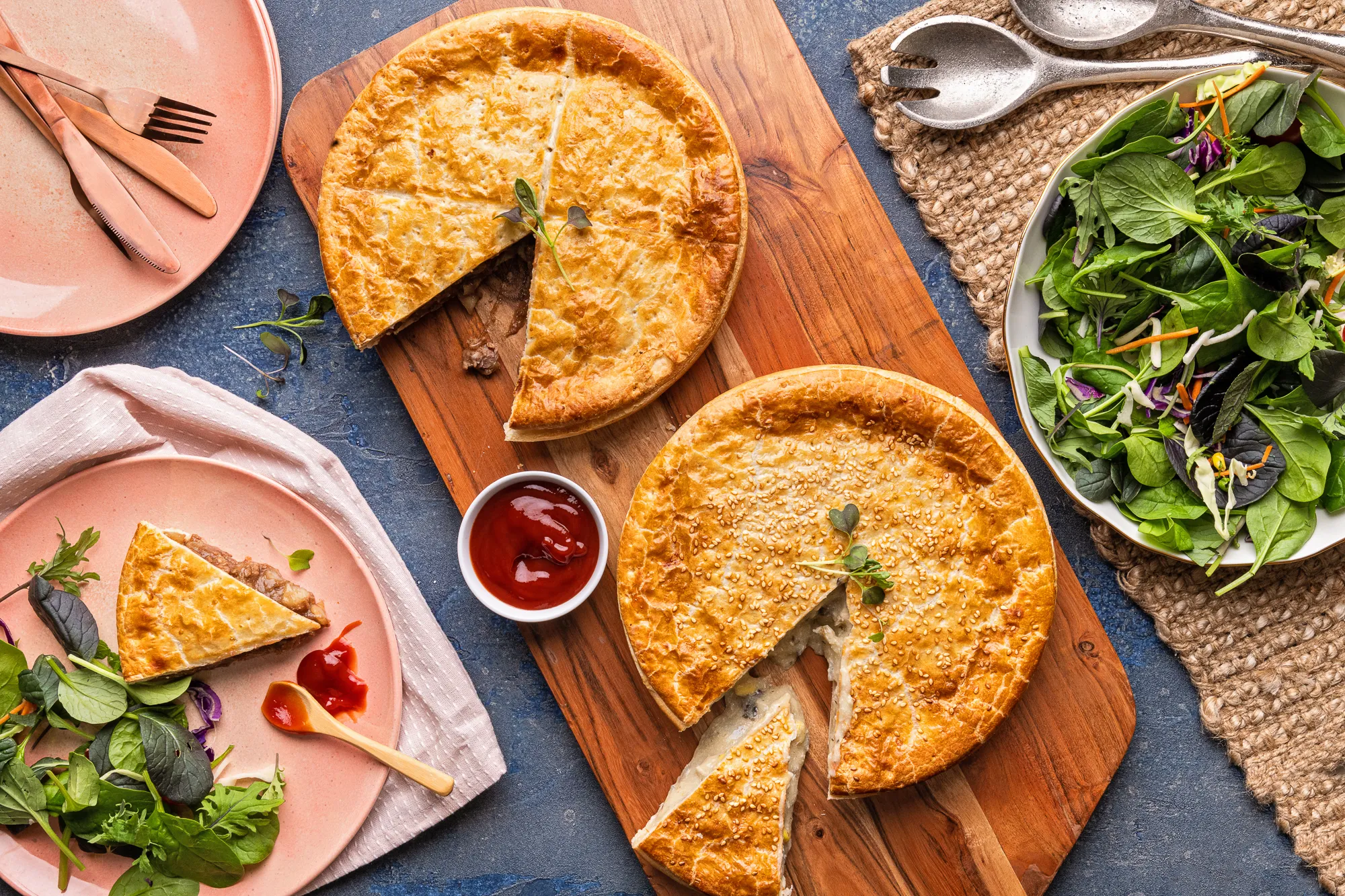 Two whole pies on a wooden board with fresh salad alongside